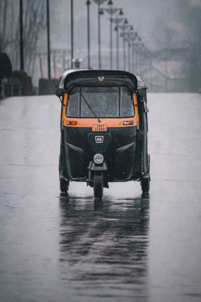 A black auto rickshaw on a wet road, showcasing rainy urban transportation.