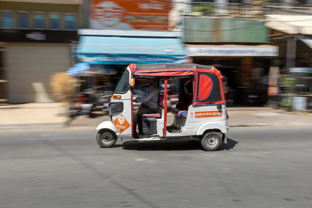 A fast-moving tuk-tuk drives through a bustling city street, capturing urban life in motion.