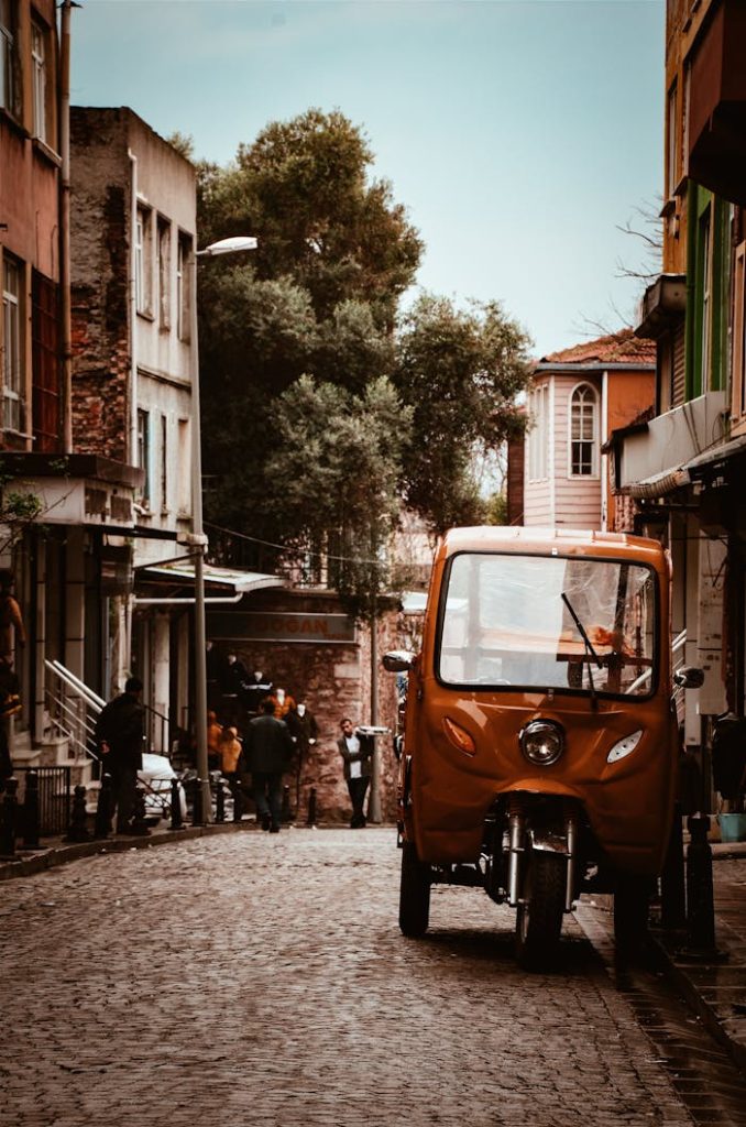 Home Colorful city street with auto rickshaw and walking people, depicting lively urban life.